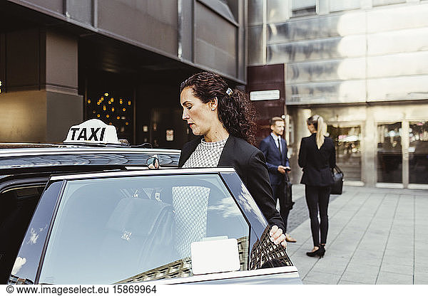 Female entrepreneur entering in taxi while coworkers standing in background