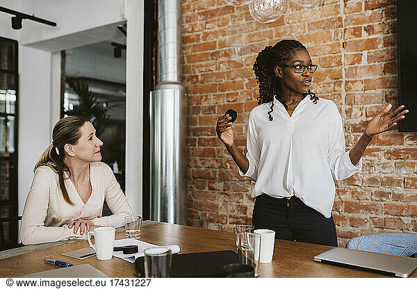 Female entrepreneur explaining product while standing by businesswoman in board room