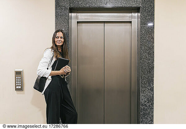 Female entrepreneur holding book while standing by elevator