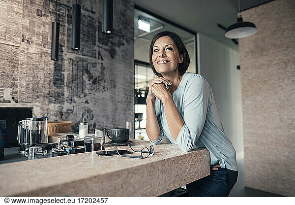 Female entrepreneur looking away while leaning on table in office