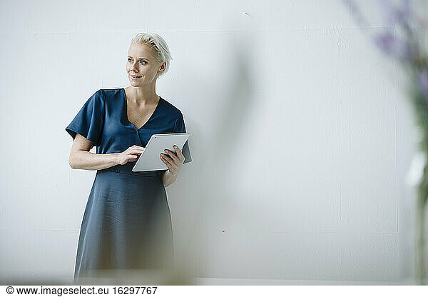 Female entrepreneur looking away while working over digital tablet against wall in office
