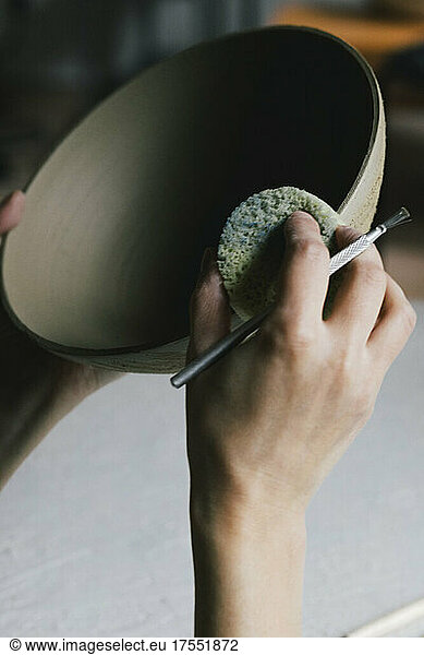 Female entrepreneur painting bowl with sponge in ceramics workshop