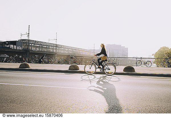 Female entrepreneur riding bicycle on street in city against sky