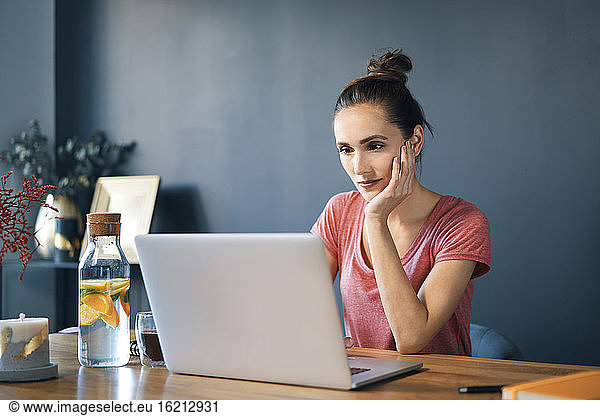 Female entrepreneur using laptop on desk against wall in home office