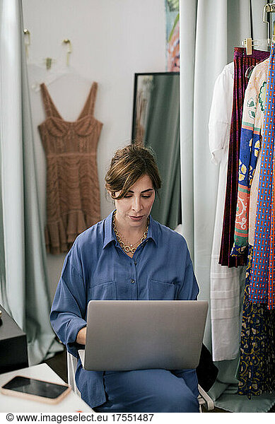 Female entrepreneur using laptop while working in clothing store