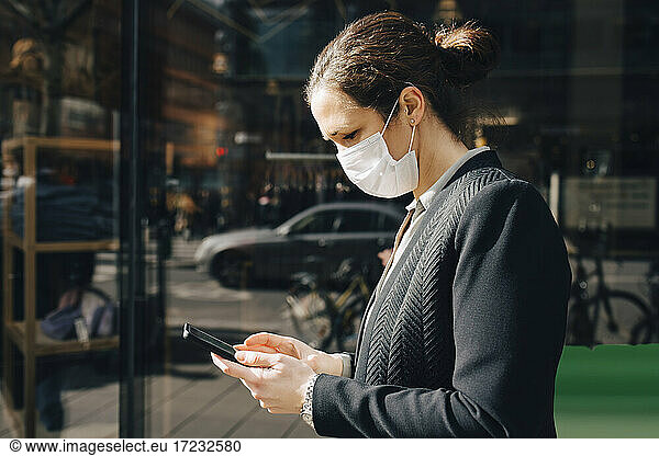 Female entrepreneur using smart phone on sunny day during pandemic