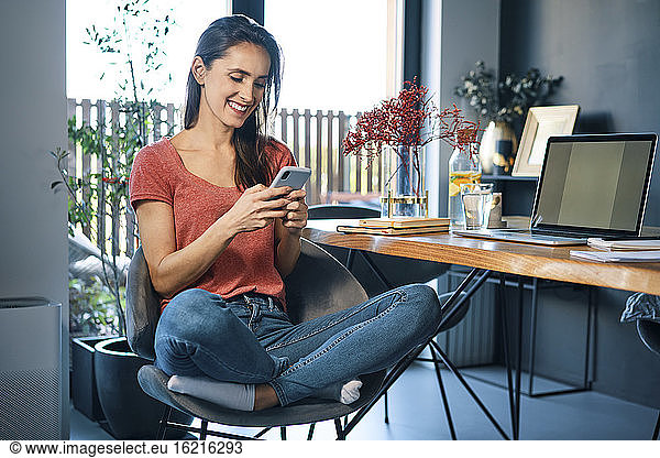 Female entrepreneur using smart phone while sitting on chair by desk in home office