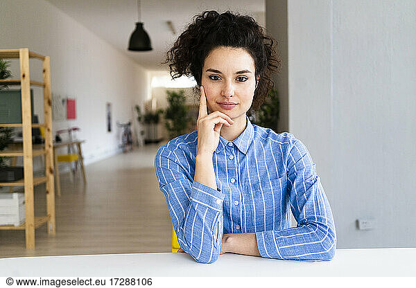 Female entrepreneur with hand on chin sitting by desk in office