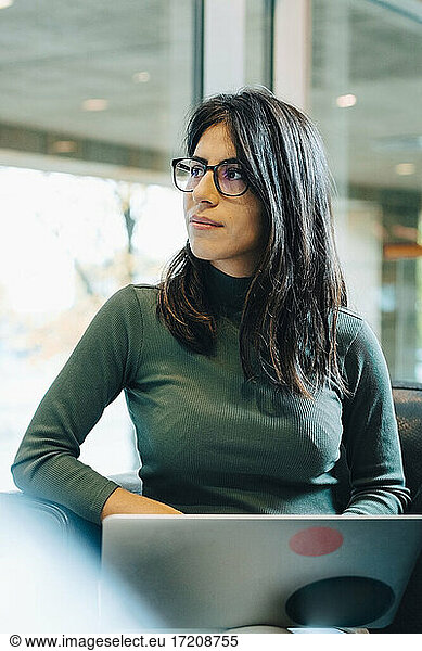 Female entrepreneur with laptop looking away in office