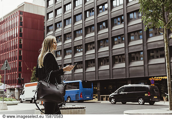 Female entrepreneur with smart phone walking against building