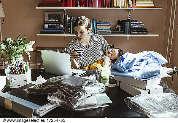 Female entrepreneur working on laptop while taking care of baby boy at home office