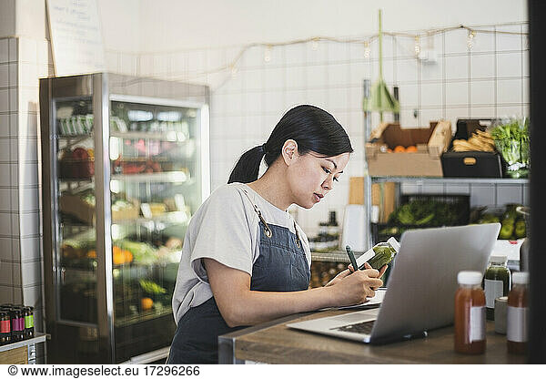 Female entrepreneur writing by laptop at store