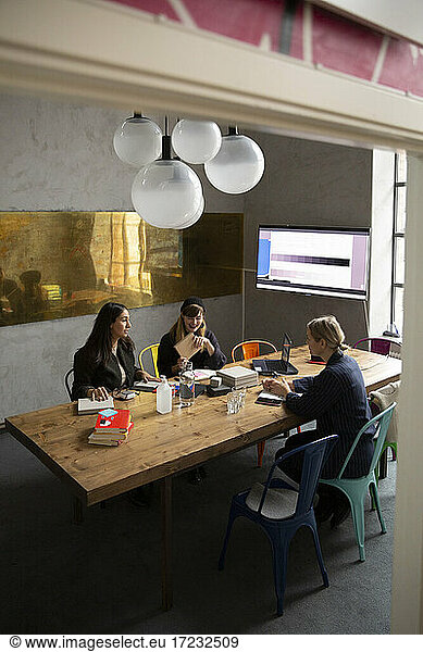 Female entrepreneurs discussing in board room seen through doorway of office