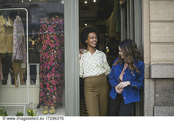 Female entrepreneurs laughing while talking with each other at clothing store