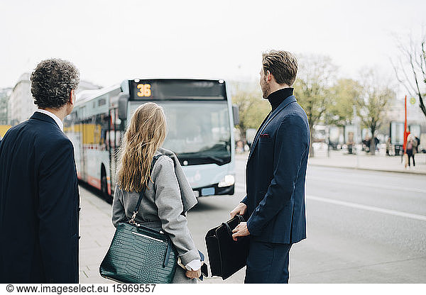 Female entrepreneurs with male coworkers looking at bus while standing in city