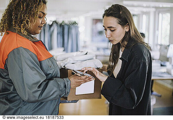 Female fashion designer receiving package from delivery person at workshop