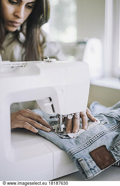 Female fashion designer sewing fabric on jeans pocket using sewing machine at workshop