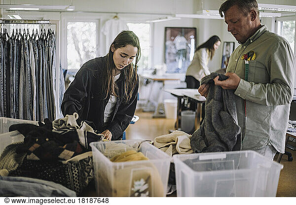 Female fashion designer with male colleague sorting recycled clothes while working at workshop