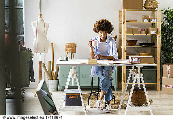 Female fashion designer with mug sitting at desk in studio