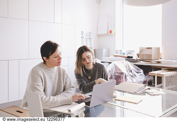 Female fashion designers discussing over laptop at desk in studio