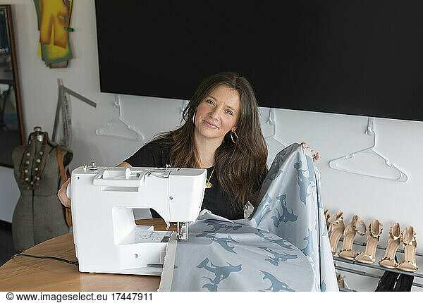 Female fashion entrepreneur sews fabric on electric sewing machine