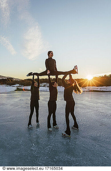 Female figure skaters practicing on frozen lake at sunset