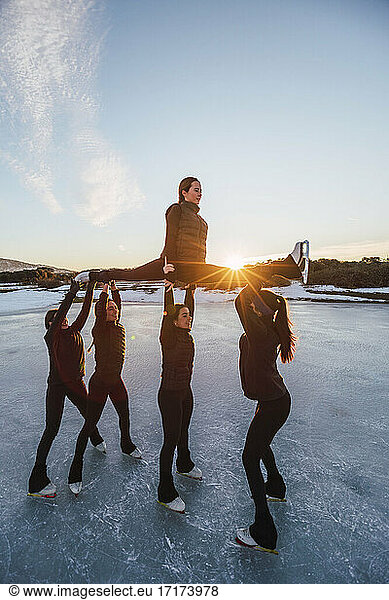 Female figure skaters practicing on frozen lake at sunset