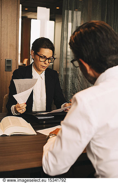 Female financial advisor reviewing documents while sitting with customer in meeting at office