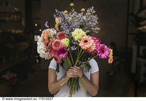Female florist holding colorful flowers while standing in shop