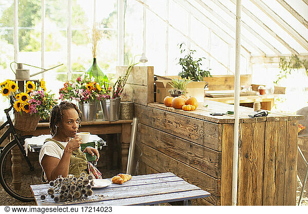 Female florist taking coffee break in flower shop greenhouse