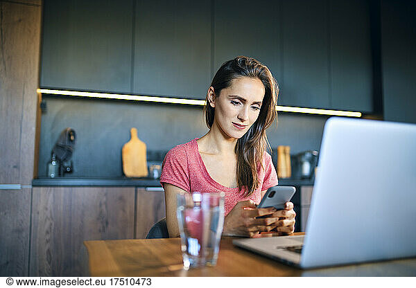 Female freelancer using mobile phone while sitting at desk in home office