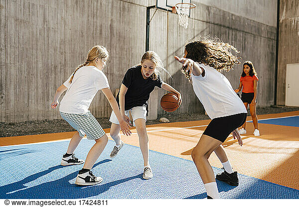 Female friends defending girl while playing basketball during competition at sports court