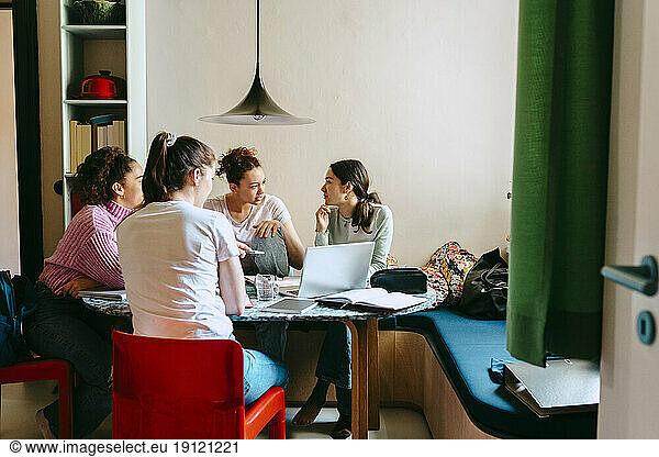 Female friends discussing while studying together at home