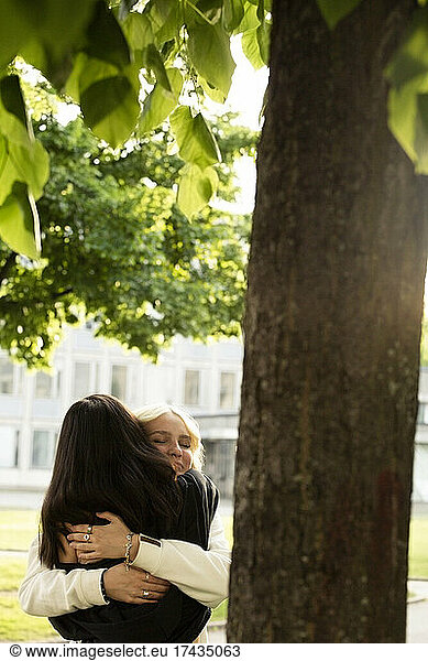 Female friends embracing by tree in park