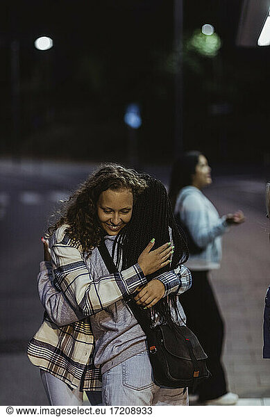 Female friends embracing each other on street at night