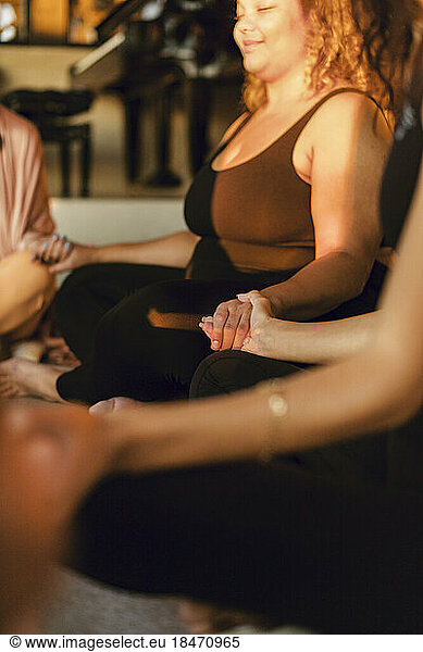 Female friends holding hands while doing meditation at retreat center