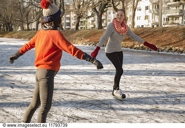 Female friends ice skating on canal