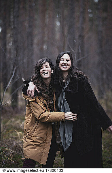 female friends laugh and hug outdoors in pine woods in germany