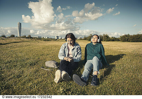Female friends listening music through headphones while spending leisure time in park