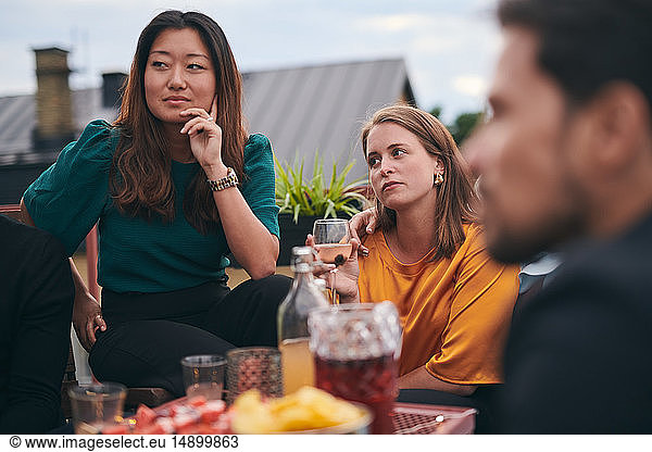 Female friends listening while looking away on terrace during social gathering