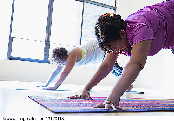 Female friends practicing downward facing dog position yoga in studio