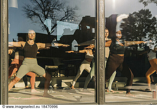 Female friends practicing yoga together at retreat center seen through glass