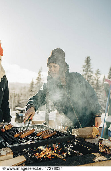 Female friends preparing sausages on barbecue grill during winter