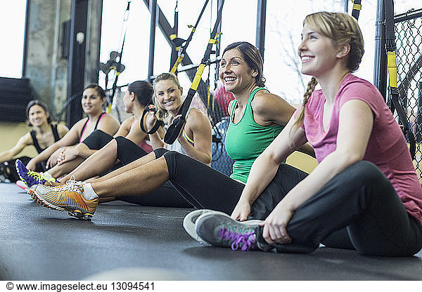 Female friends relaxing while sitting by resistance bands in gym