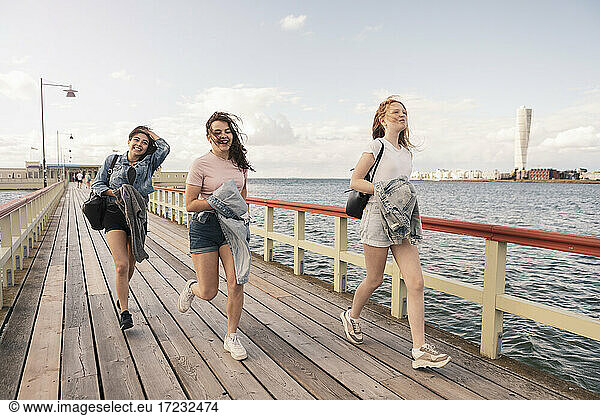 Female friends running on pier by sea against sky