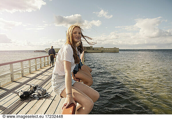 Female friends sitting over railing amidst sea against sky