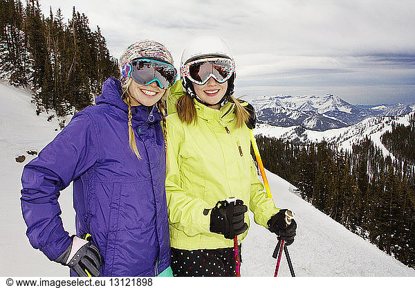 Female friends skiing on snow covered field against mountains