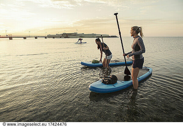 Female friends standing by paddleboard in sea