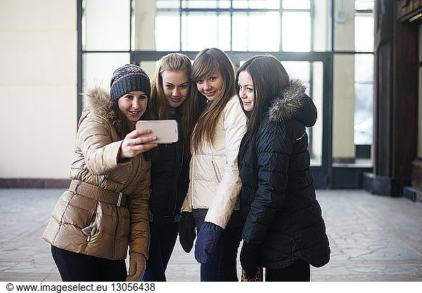 Female friends taking selfie through smart phone while standing outside building