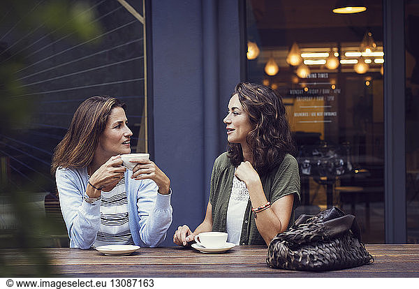 Female friends talking while having coffee at sidewalk cafe